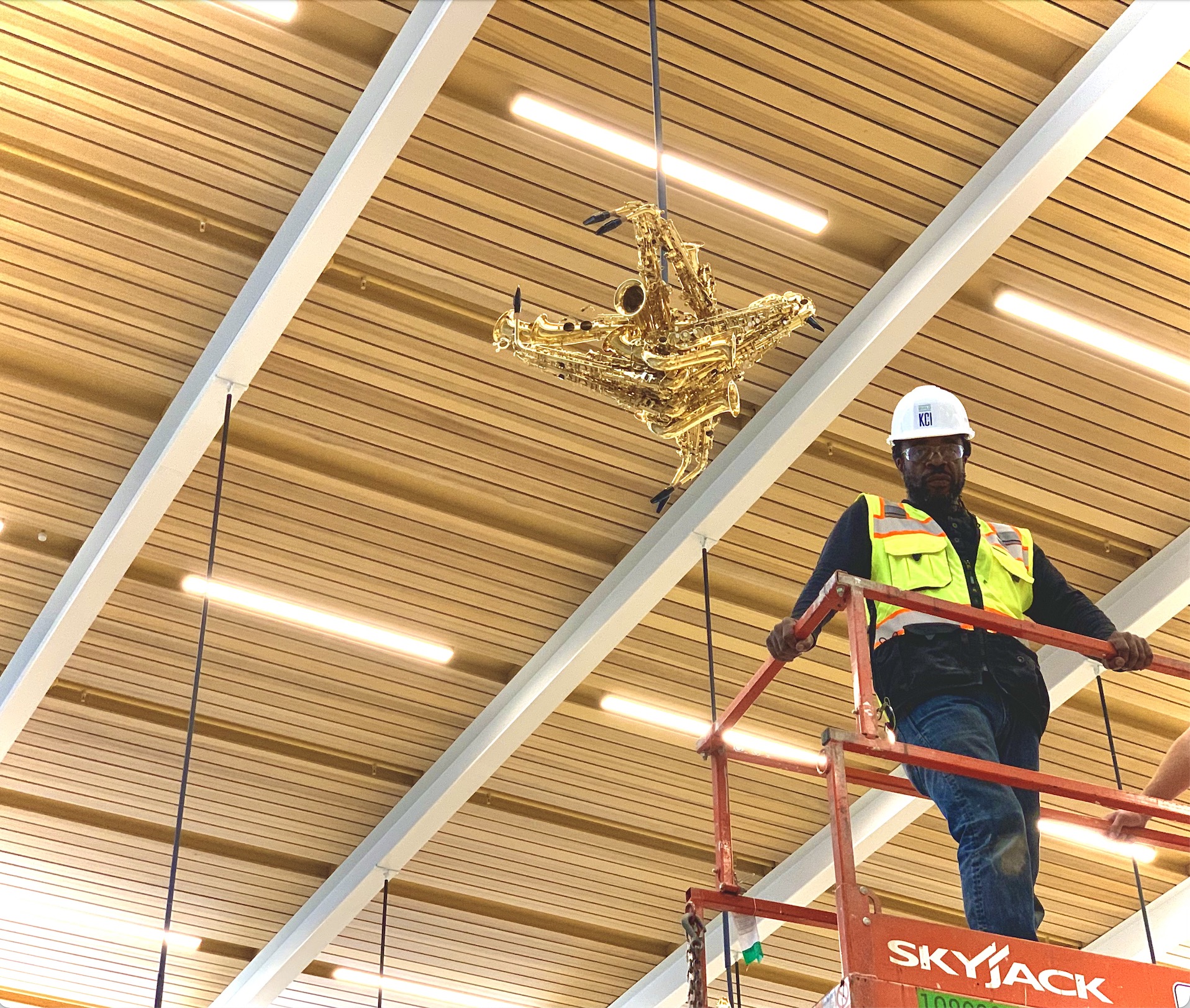 Installer on a lift raising a saxophone-bird sculpture