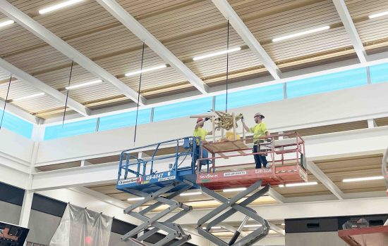 Installers on a scissor lift securing a sculpture to the ceiling
